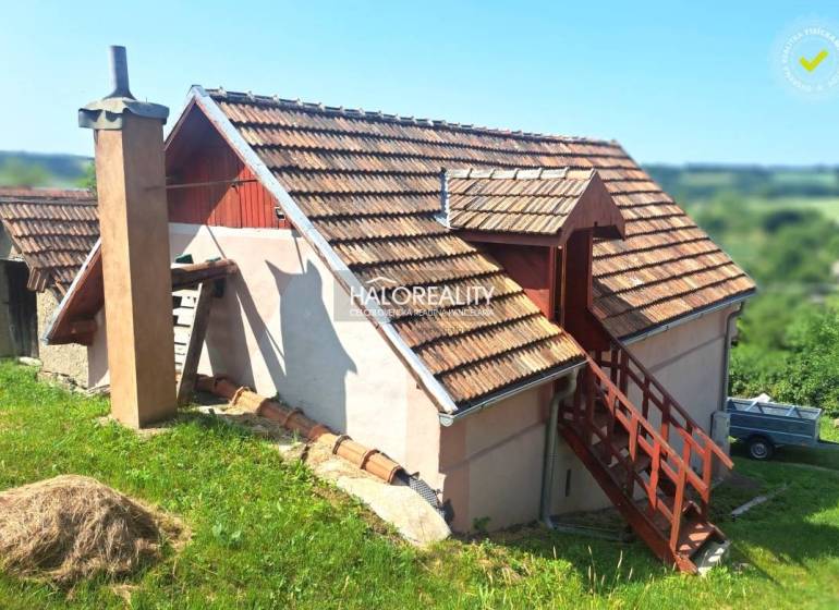 A cottage in Hontianske Trsťany with a wooden roof and an external staircase surrounded by nature.