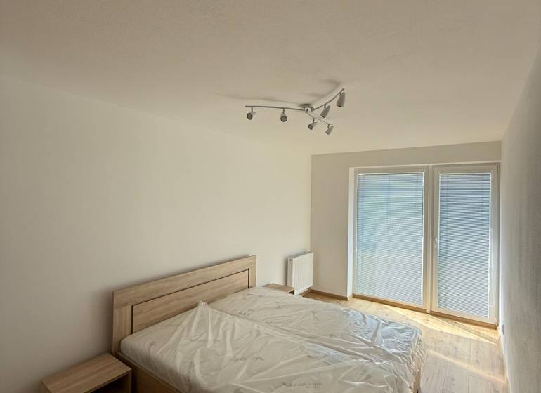 A bedroom in a two-room apartment with a bed and a nightstand, a spacious window with blinds.