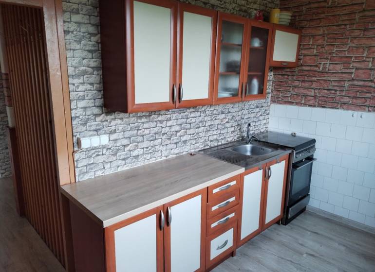A kitchen in a 2-room apartment with cabinets and equipment, brick wall appearance.