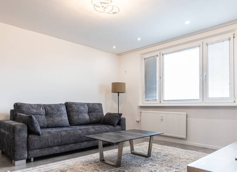 Living room with a dark sofa, coffee table, and floor lamp in a three-room apartment.