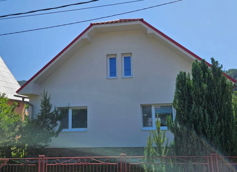 A family house in Liptovská Osada with a sloped roof and a fence surrounded by greenery.
