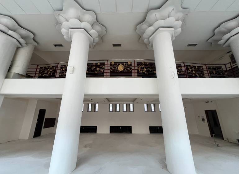Interior of commercial spaces with large columns and decorative railing on the upper floor.