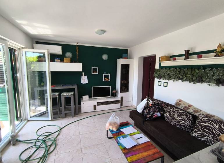 Living room in a two-room apartment with a dark sofa, decorations, and open glass doors.