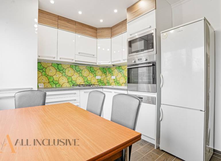 A kitchen in a 3-room apartment with colorful tiles, a white refrigerator, and a wooden table.