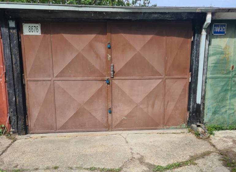 A garage in Hagarov with brown doors and the number 8676, surrounded by greenery.