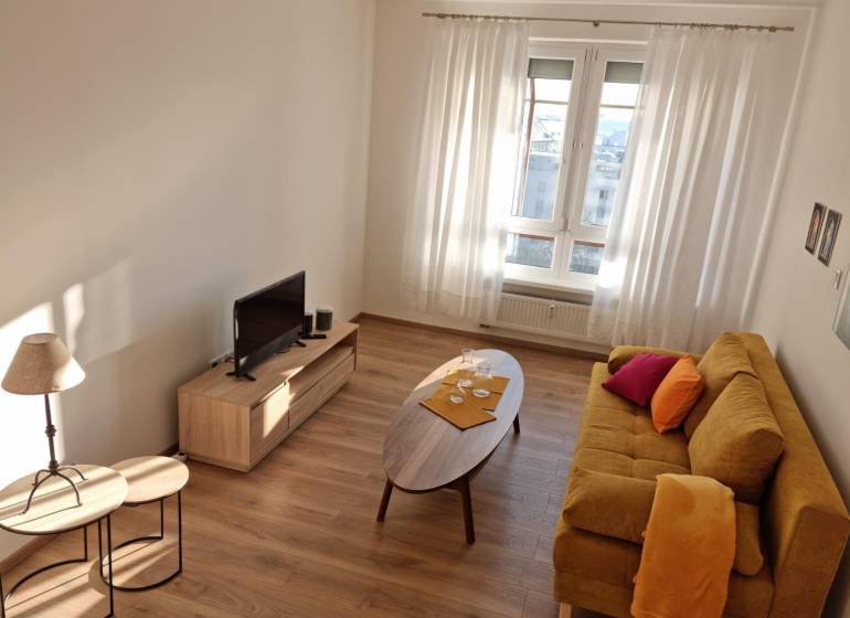 Living room in a two-room apartment with a yellow sofa, TV stand, and wooden tables.
