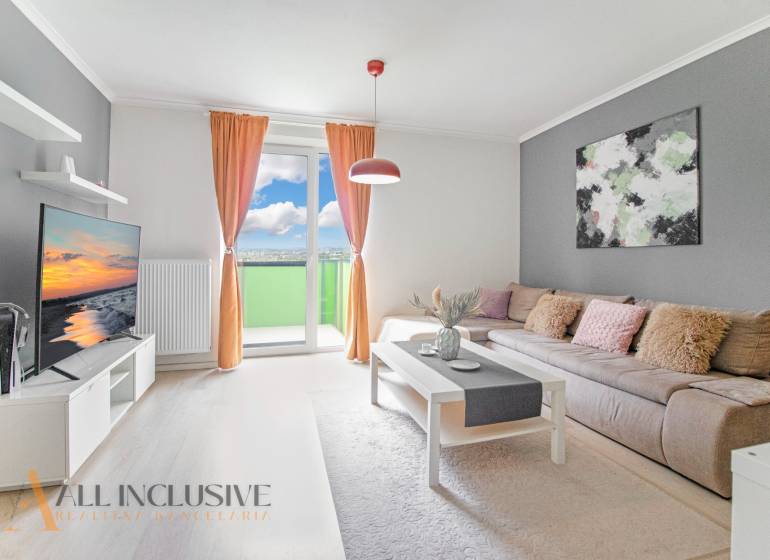 Living room of a two-room apartment with a sofa, television, and balcony, light curtains and accessories.