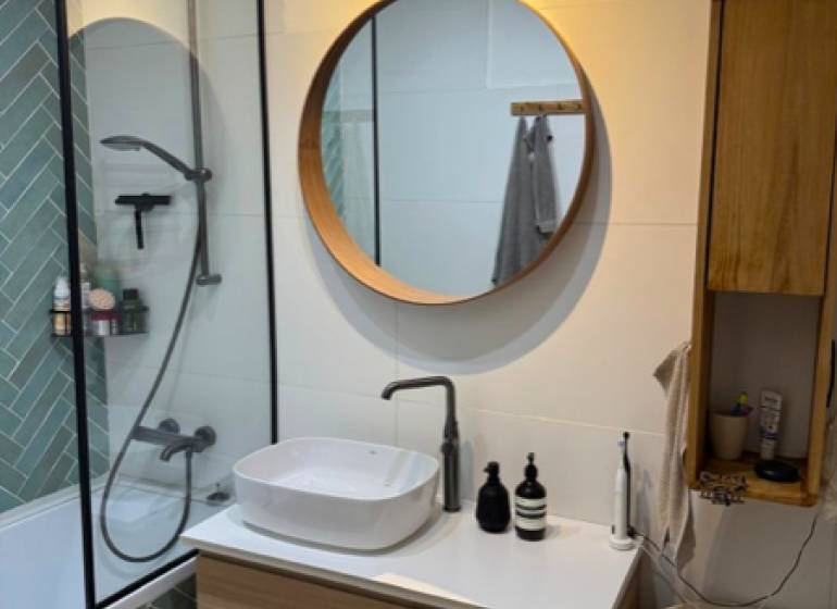 A bathroom in a 4-room apartment with a wooden sink and a round mirror.