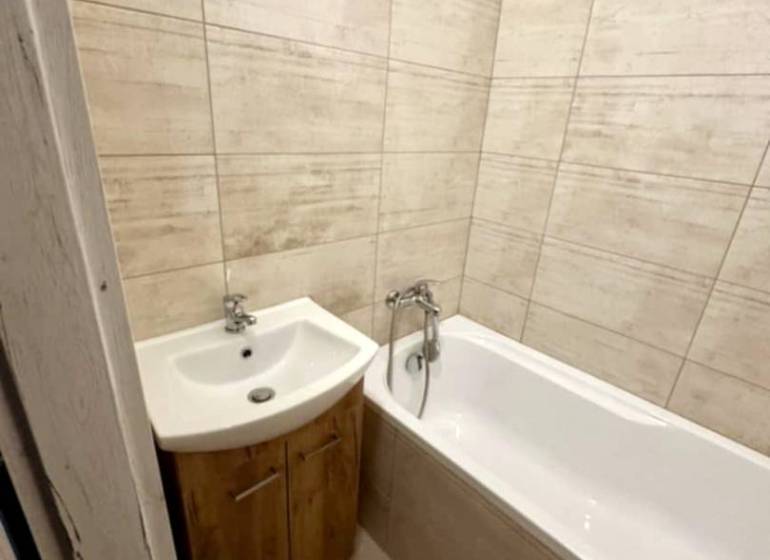 Bathroom in a 2-room apartment with a bathtub and a sink in a wooden decor.