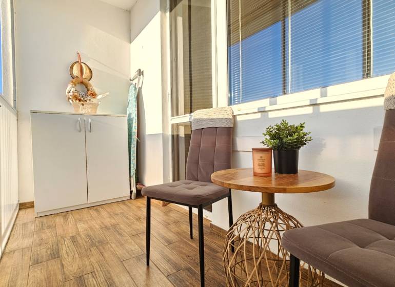 A balcony in a one-room apartment with two chairs, a table, and a storage cabinet.