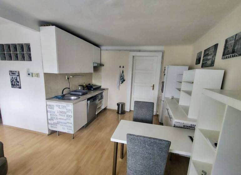 A kitchen in a 2-room apartment with a dining table, white cabinets, and wooden flooring.