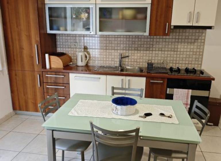 A kitchen in a 2-room apartment with wooden cabinets and a dining table with four chairs.