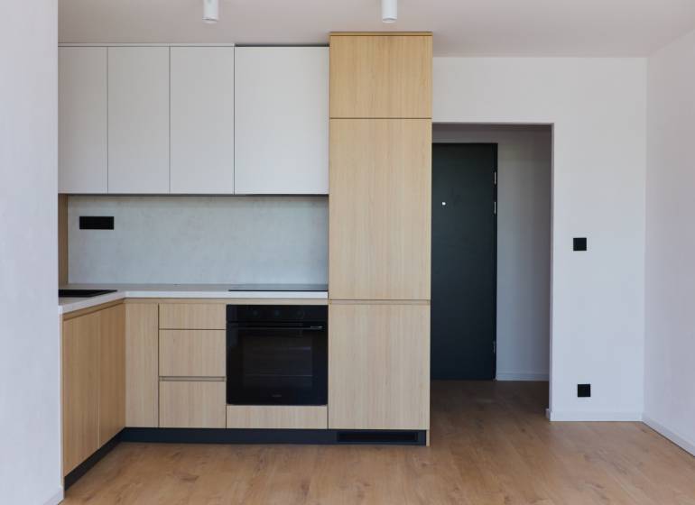 A kitchen in a 2-room apartment with wooden cabinets and black appliances.