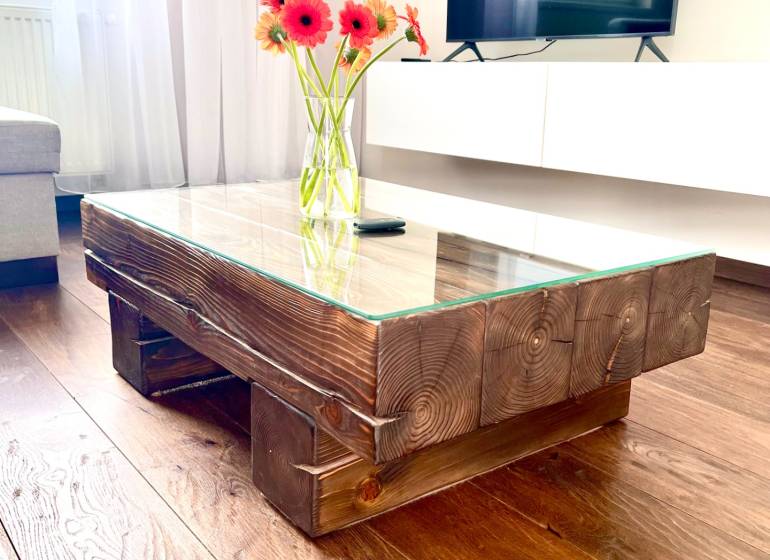 Glass table with a wooden frame and flowers in a vase in a 2-room apartment.