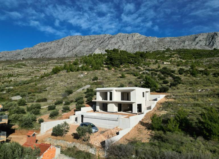 A villa in Duće surrounded by greenery and mountains with a blue sky in the background.