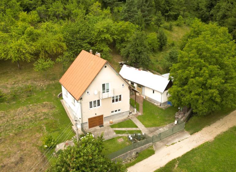 A family house in Papradno surrounded by a grassy plot and trees, access road.