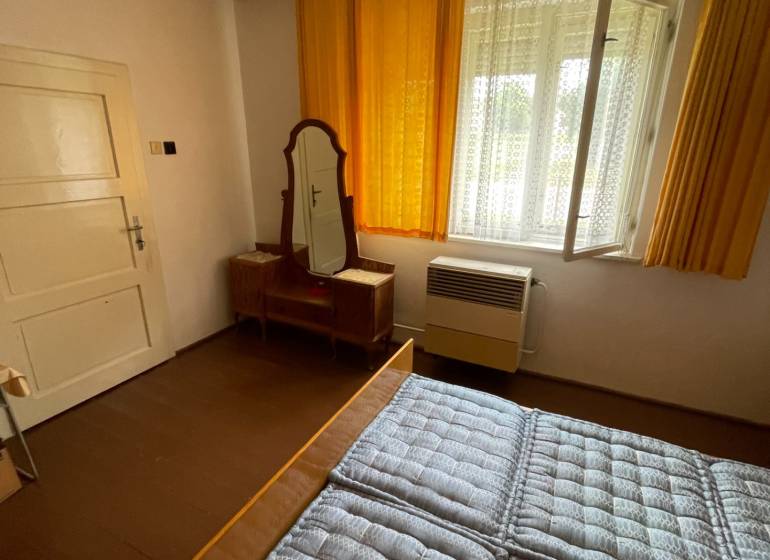 Bedroom in a family house with a window, a mirror, and a bed with a quilted mattress.