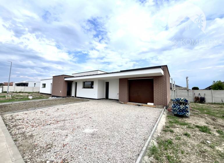 A family house in Miloslavov with a brick facade and a large parking lot, clear sky.