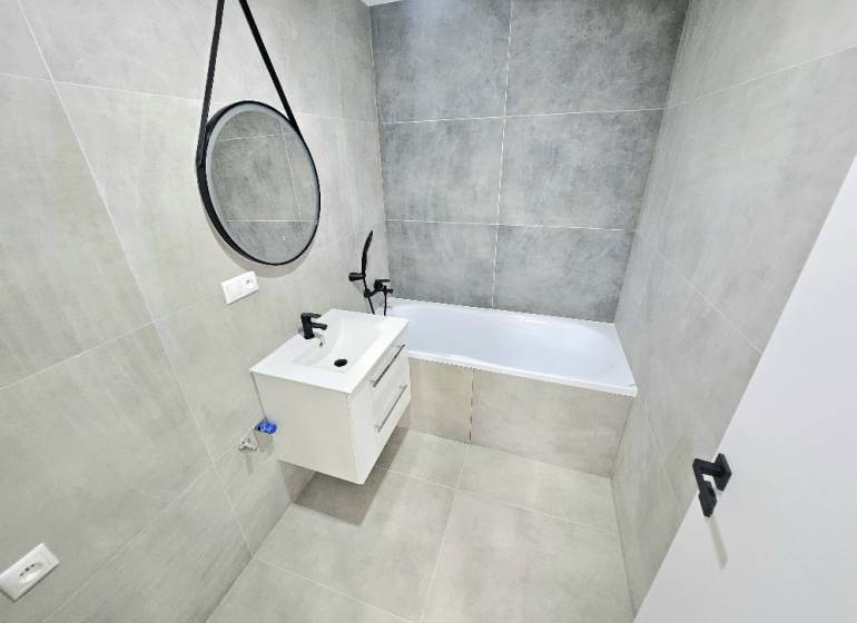 A bathroom in a 3-room apartment with a bathtub, a sink, and a mirror on the wall.