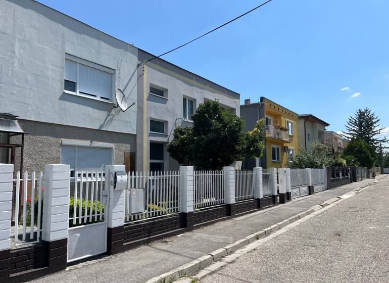 A street with family houses in Komárno, with a white fence and a satellite dish.