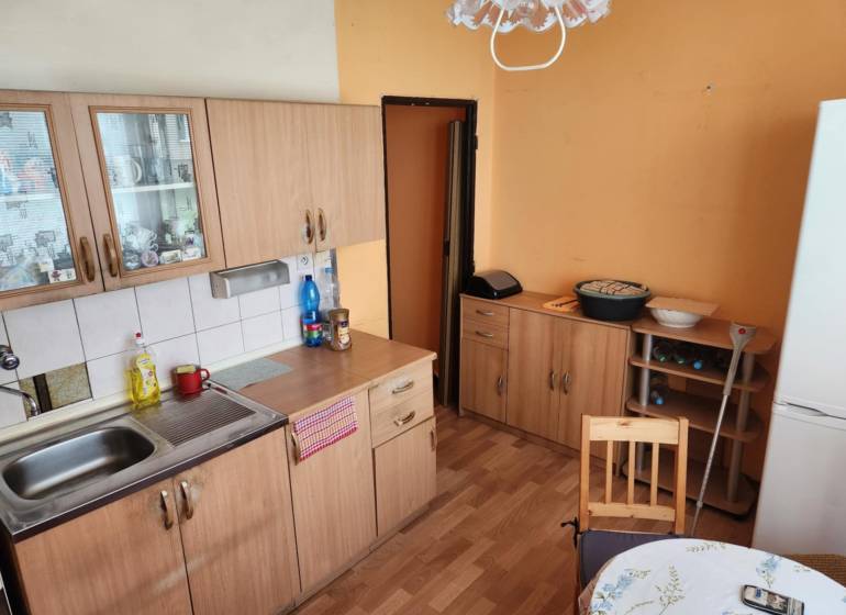 A kitchen in a studio apartment with wooden cabinets, a table, and a refrigerator.