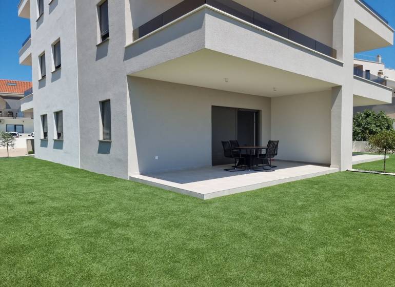 The exterior of a 4-room apartment in Vodice with a modern terrace and green lawn.