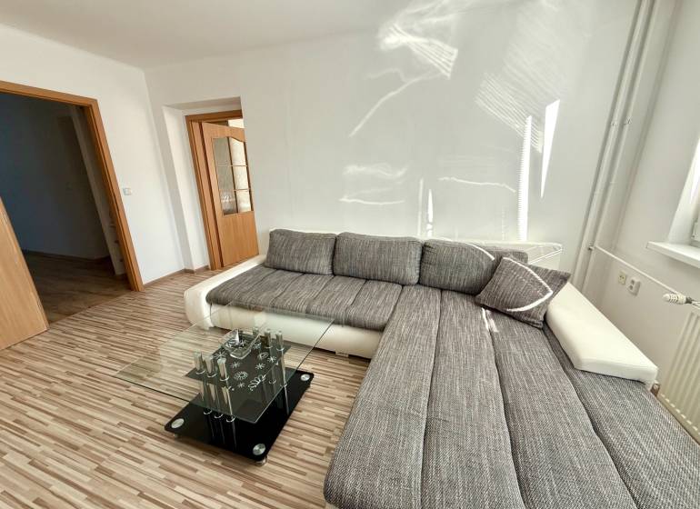 A bright living room with a corner sofa and a glass table in a two-room apartment.