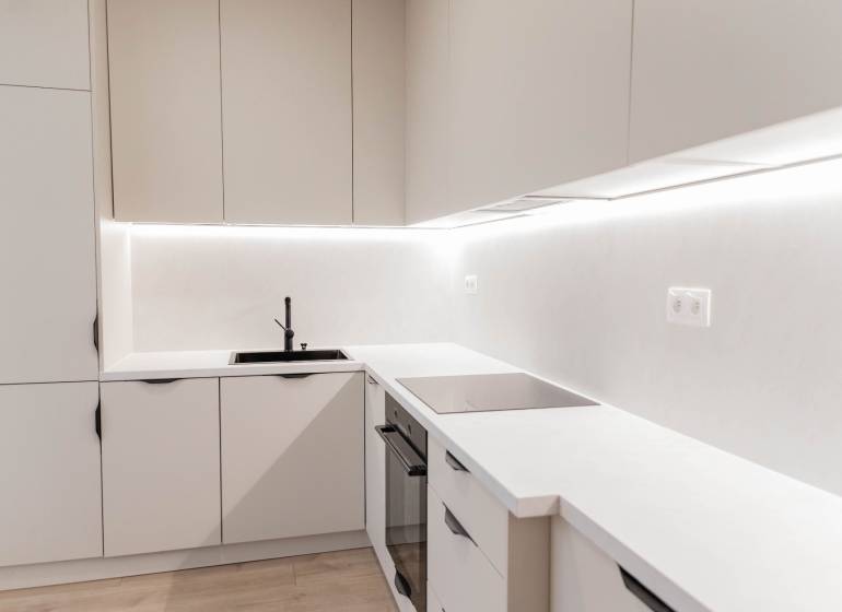 A kitchen in a 2-room apartment with white cabinets and a black sink.