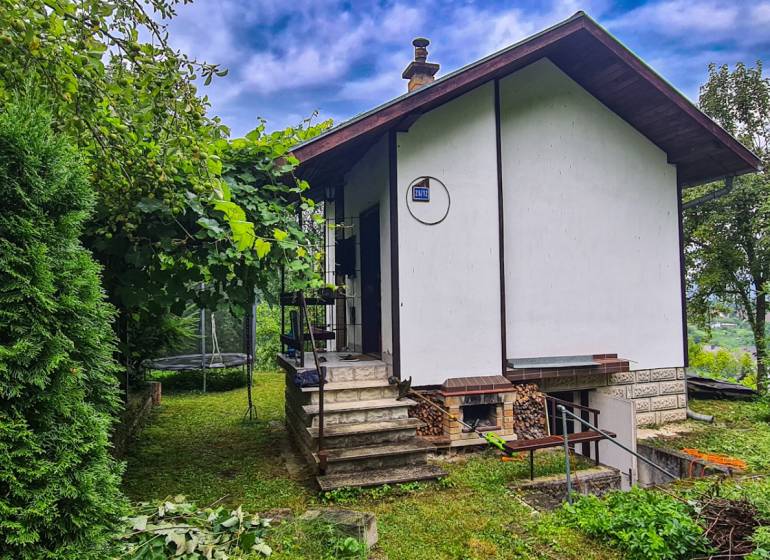 A cottage in Mojš surrounded by greenery, stairs leading to the entrance, a trampoline in the garden.