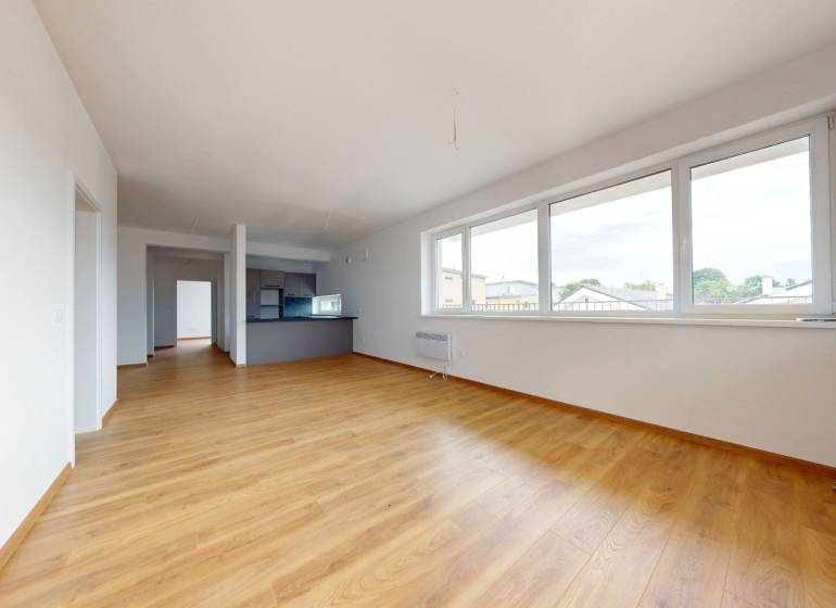 A spacious living room with wooden flooring and large windows in a 3-room apartment.