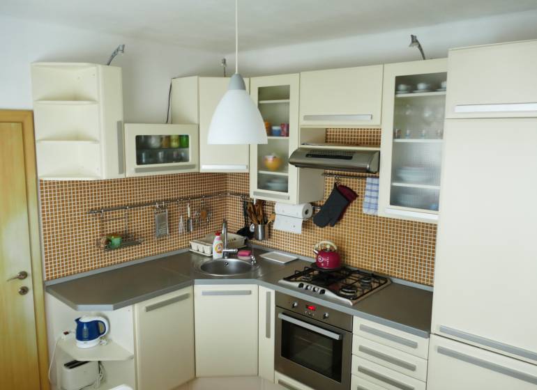 A kitchen in a 3-room apartment with a kitchen unit, appliances, and orange tiles.