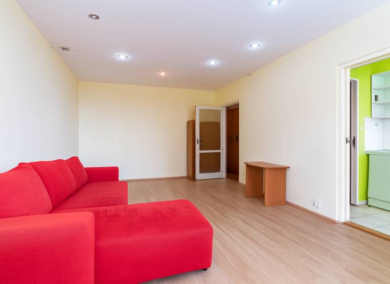 Living room with a red sofa, wooden floors, and doors to the kitchen.
