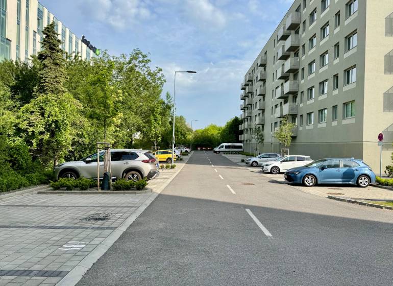 A road with cars and greenery in Bratislava-Trnávka on Ivánska Road, next to residential buildings.
