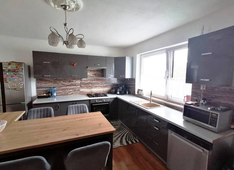 A kitchen in a family house with dark furniture, spacious windows, and a wooden table.