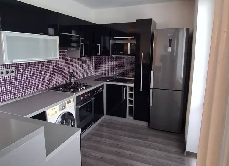 A kitchen in a 2-room apartment with appliances, dark furniture, and purple tiles.