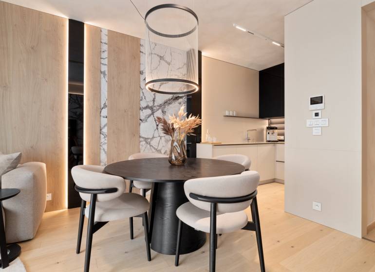 Dining room in a 3-room apartment with a round table, wooden decorations, and an open kitchen.