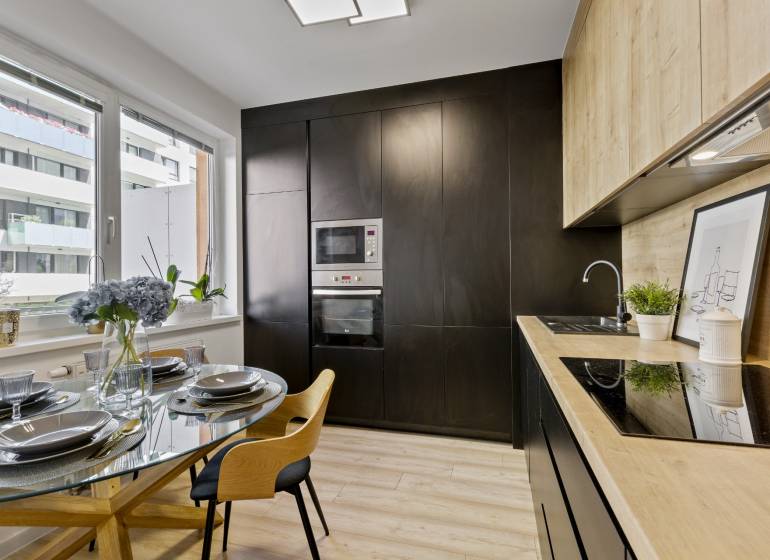 A kitchen in a 2-room apartment with a dining table and a modern black kitchen unit.