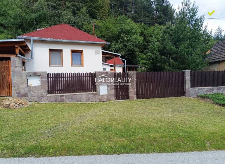 A cottage in Helcmanovce with a wooden fence and a manicured lawn surrounded by greenery.