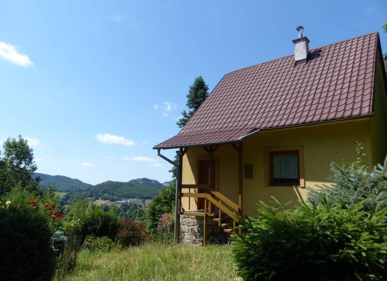 A cottage in Štiavnické Bane, surrounded by greenery and with a view of the hills in the background.