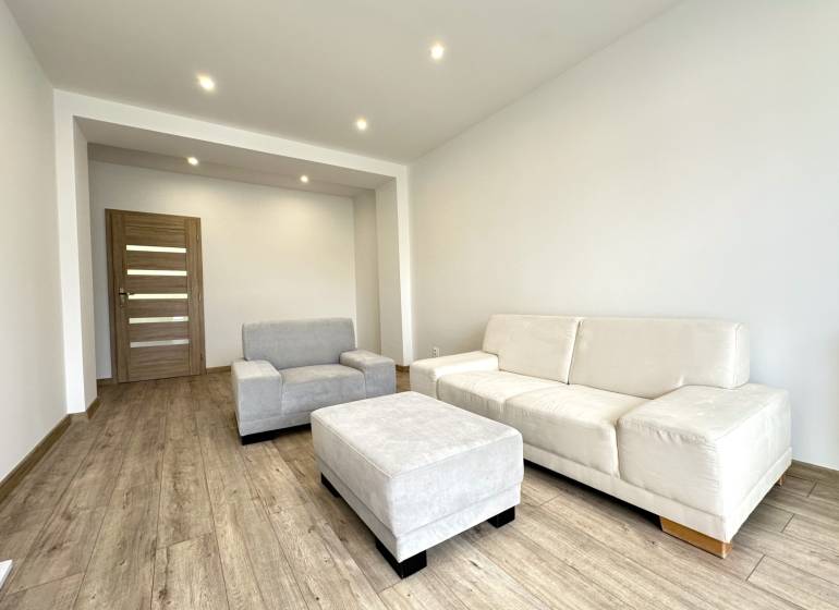A bright living room in a two-room apartment with beige furniture and wooden flooring.