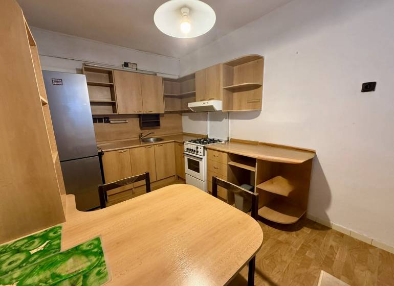 A kitchen in a one-room apartment equipped with wooden furniture and a refrigerator.