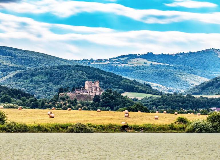 Picturesque scenery of agricultural and forest lands near Lučenec with castle ruins in the middle.