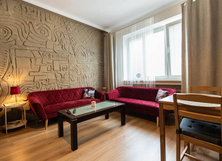 Living room in a two-room apartment with a patterned wall and red sofas.