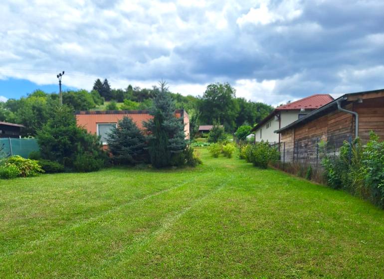 A grassy plot for living in the village of Bodovce surrounded by houses and trees.