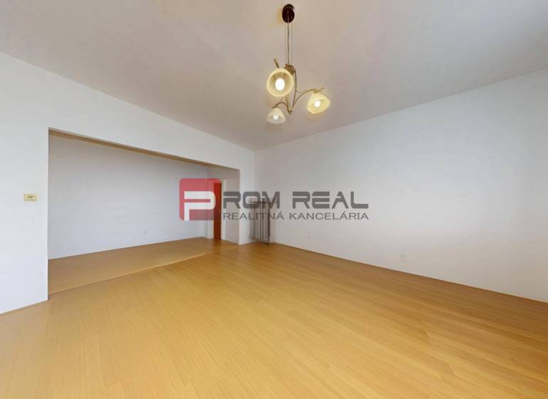 A spacious room with wooden flooring and a light fixture in a 3-room apartment.