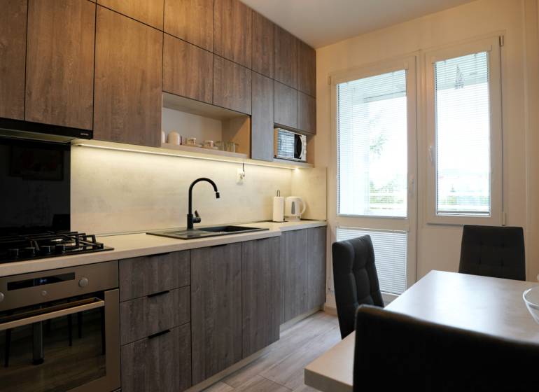 A kitchen with wooden cabinets, a gas stove, and a dining table in a 2-room apartment.