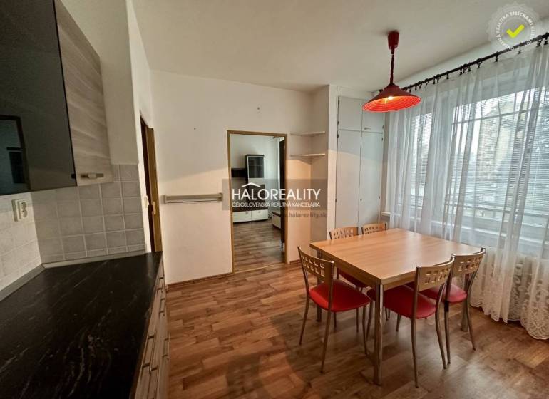 Dining room in a one-bedroom apartment with wooden floors and a large window with lace curtains.