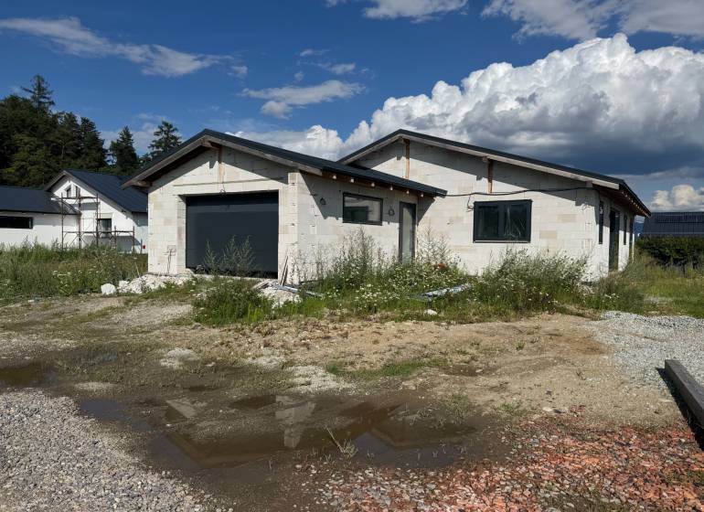 An unfinished family house in Valča with a garage, surrounded by nature and construction materials.
