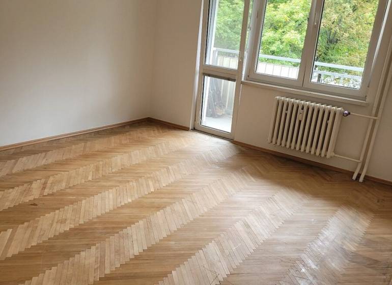 A room in a 3-room apartment with wooden flooring and balcony doors.