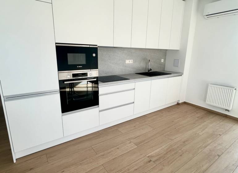 A kitchen in a 3-room apartment with white cabinets, appliances, and wooden flooring.
